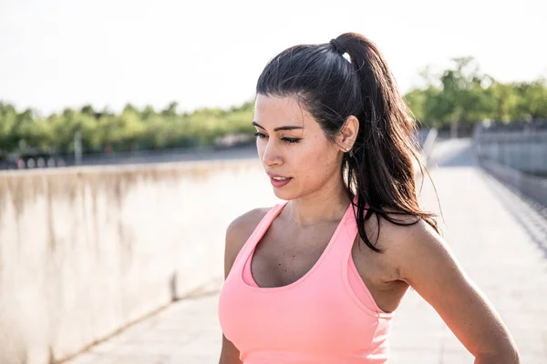 Latin woman with ponytail in her hair gets ready to go for a run. Dress a pink body