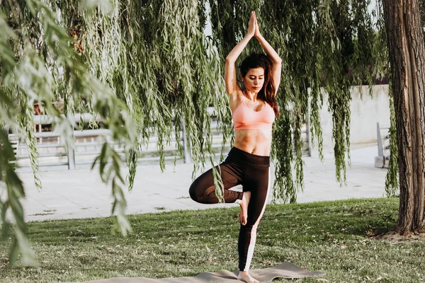 Latin woman does yoga exercises in a park in Madrid. Balance and concentration