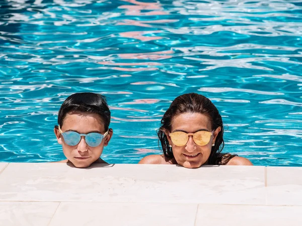 サングラスをかけた母と息子は、晴れた夏の日にプールの端に寄りかかっています. — ストック写真