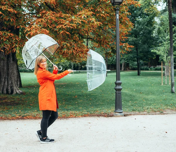 Καυκάσια κοπέλα σε κόκκινο καμπαρντίνα παίζει με δύο διαφανείς ομπρέλες σε ένα πάρκο — Φωτογραφία Αρχείου