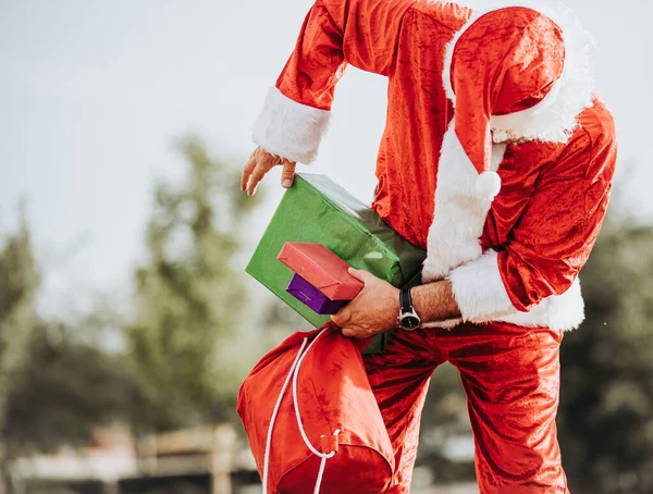 Foto stock de Papai Noel sem barba de pé colocando presentes em um saco vermelho. Tempo de Natal — Fotografia de Stock