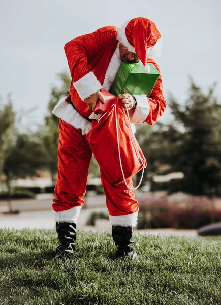 Foto stock de Papai Noel sem barba de pé colocando presentes em um saco vermelho. Tempo de Natal — Fotografia de Stock