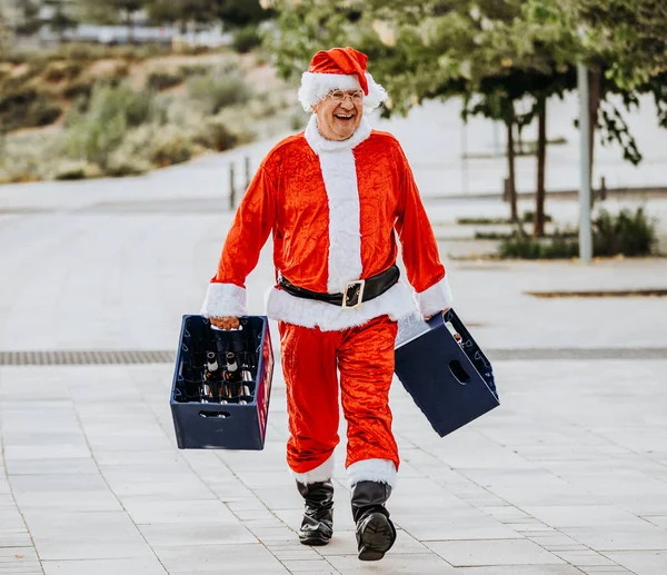 Vertical stock photo of papa noel without beard loading with two boxes of beer. Christmas time