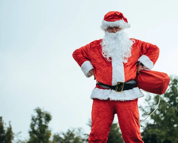 Papai Noel de pé com os braços apoiados em seus quadris agarrando seu saco vermelho — Fotografia de Stock