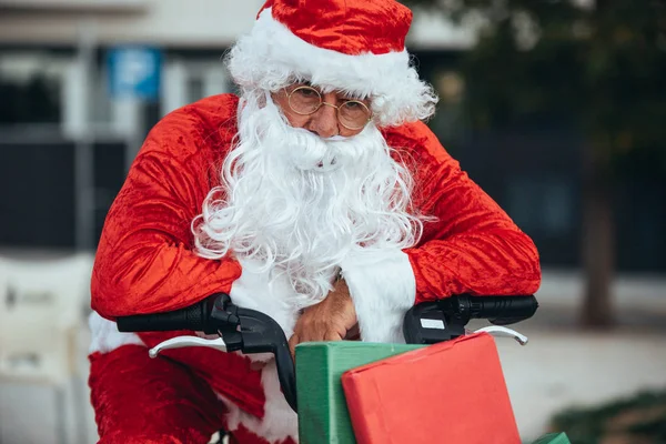 Noel Baba 'nın dikey fotoğrafı. Yorgun bir ifadeyle hediyelerle dolu bir bisikletle destekleniyor. Noel zamanı