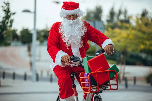 Zdjęcie Świętego Mikołaja z prezentami w rowerze i jego czerwoną walizką na plecach. Czas Bożego Narodzenia — Zdjęcie stockowe