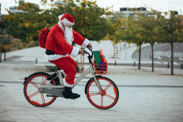 Stock photo of Santa Claus with gifts in the bicycle and his red suitcase on his back. Christmas time