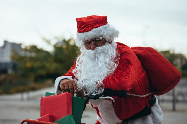 Foto de estoque vertical de Papai Noel apoiado em uma bicicleta cheia de presentes com expressão exausta. Tempo de Natal — Fotografia de Stock