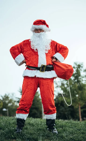 Foto stock de Papai Noel de pé com os braços apoiados em seus quadris agarrando seu saco vermelho. Tempo de Natal — Fotografia de Stock