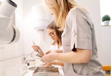 Modern diş sağlığı kliniğinde çalışırken, tıbbi üniformalı kadınların temiz aletleri prosedür için hazırlayışının yan görüntüsü