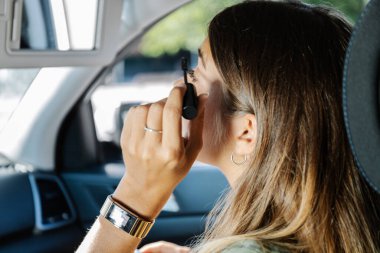 Kadın somurtuyor ve arabanın yolcu koltuğunda otururken yanağına ruj sürüyor.