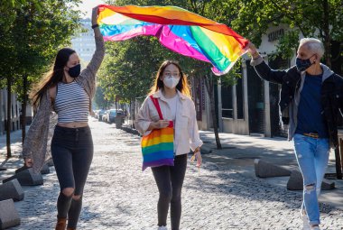 Madrid caddesinde renkli LGBT bayrağı ve gökkuşağı çantasıyla yürüyen koruyucu maskeli neşeli etnik gruptan oluşan bir grup.