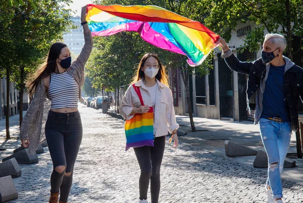 カラフルなLgbtの旗と虹の袋でマドリードの街を歩く保護マスクの陽気な多民族の人々のグループ — ストック写真