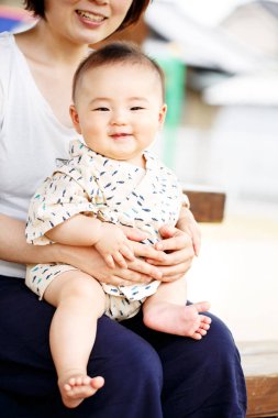 Diz üzerinde açık havada bir bankta bir bebek tutan güzel bir genç anne.