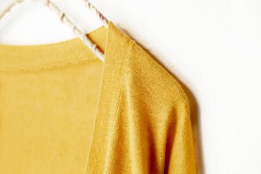 Beyaz arka plan üzerinde elbise askısı sarı asılı bir hırka.