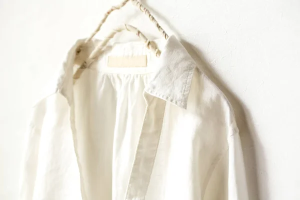 En blus eller skjorta i vit hänger på galge på vit bakgrund. Närbild. — Stockfoto