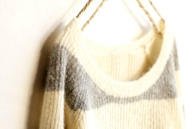 Beyaz ve gri çizgili süveter beyaz arka planda asılı. Yaklaş..