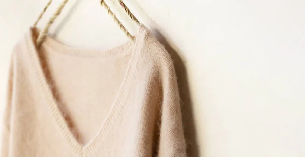 light pink sweater hanging on clothes hanger on white background.