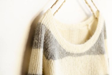 Beyaz ve gri çizgili süveter beyaz arka planda asılı..