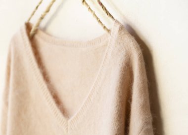 beyaz arka plan üzerinde giysi askısı asılı açık pembe kazak.