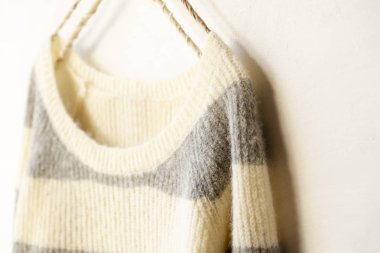 Beyaz ve gri çizgili süveter beyaz arka planda asılı..