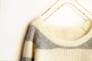 Beyaz ve gri çizgili süveter beyaz arka planda asılı..