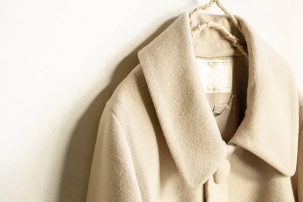Abrigo de lana beige colgando de la percha de ropa sobre fondo blanco — Foto de Stock
