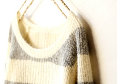 Beyaz ve gri çizgili süveter beyaz arka planda asılı..