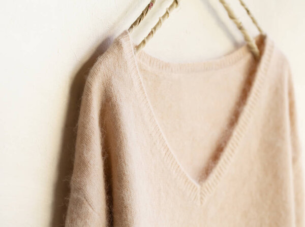 светло-розовый свитер висит на вешалке для одежды на белом фоне
.