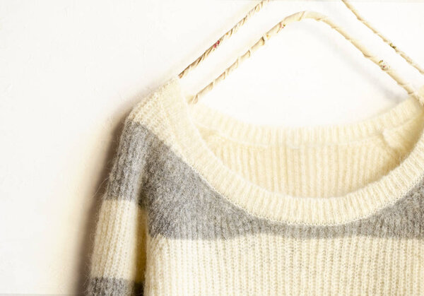 Белый и серый полосатый свитер висит на вешалке для одежды на белом фоне
.