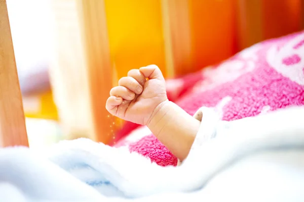 Hand of an energetic newborn baby with light blue and pink blanket and baby bed. — Stock Photo, Image