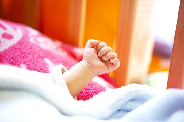 Hand of an energetic newborn baby with light blue and pink blanket and baby bed. — Stock Photo, Image