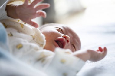 Sevimli yeni doğmuş bebek yatakta yatıyor, ağlıyor. Yakın çekim.