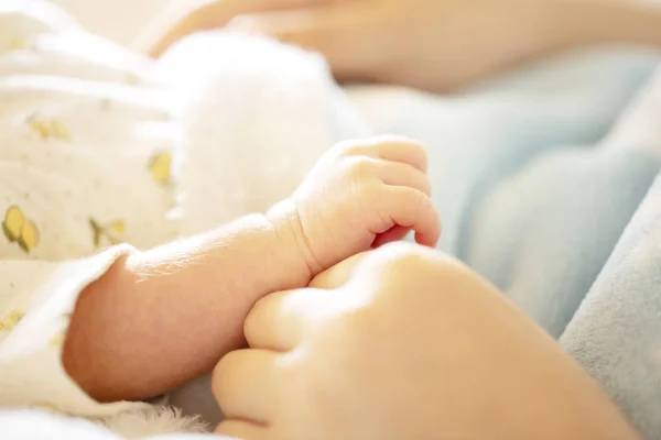 Mão de bebê recém-nascido nas mãos da mãe com cobertor azul claro macio . — Fotografia de Stock
