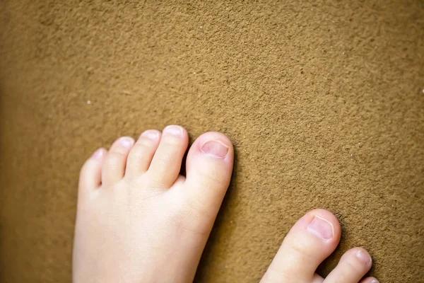 Barns nakna fötter. Barnets nakna fötter på brun bakgrund. — Stockfoto