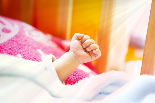 一个精力充沛的新生儿的手与浅蓝色和粉红色的毯子和婴儿床. — 图库照片