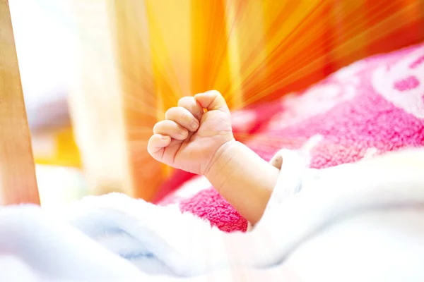 Hand of an energetic newborn baby with light blue and pink blanket and baby bed. — Stock Photo, Image
