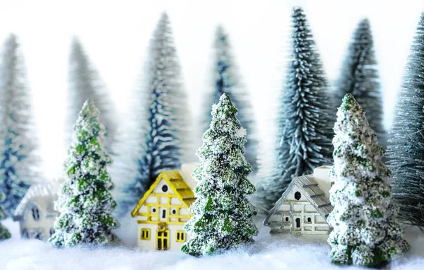 Mini zasněžené vánoční stromky s domy v lese. Bokeh, pozadí světel. — Stock fotografie