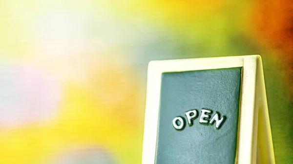 Närbild av en grön med gul "Öppna" tavlan skylt lutande mot ljus med färgglada bakgrund. — Stockfoto