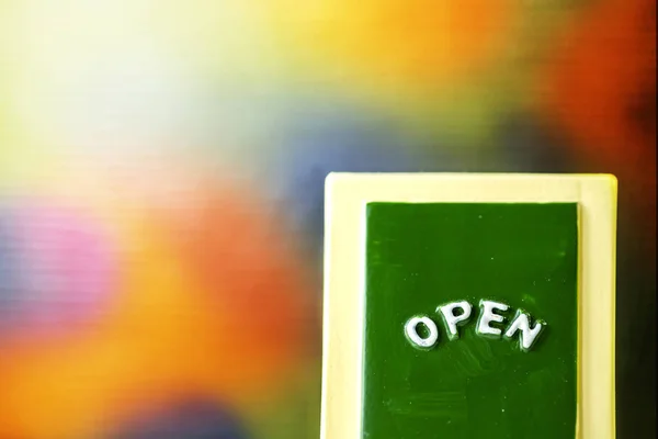 Close-up de um verde com amarelo sinal "ABERTO" quadro inclinando-se contra brilhante com fundo colorido . — Fotografia de Stock