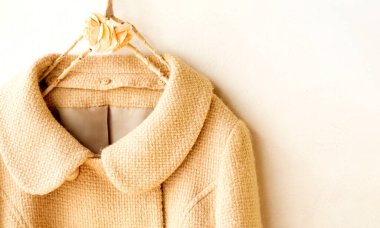 Elbiselerde asılı bej renkli yün palto. Beyaz arka planda asılı. Kapat..