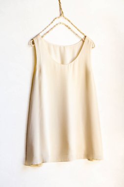 Beyaz bir duvarda asılı açık bej ya da beyaz bir bluz. Yaklaş.