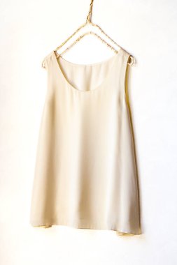 Beyaz bir duvarda asılı açık bej ya da beyaz bir bluz. Yaklaş.