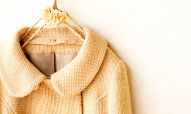 Elbiselerde asılı bej renkli yün palto. Beyaz arka planda asılı. Kapat..