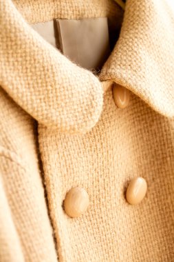 Elbiselerde asılı bej renkli yün palto. Beyaz arka planda asılı. Kapat..
