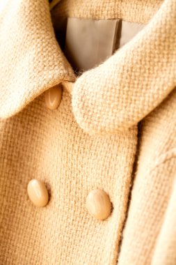 Elbiselerde asılı bej renkli yün palto. Beyaz arka planda asılı. Kapat..