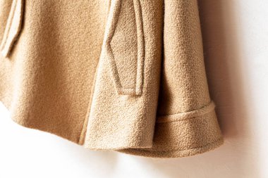 Elbiselerde asılı bej renkli yün palto. Beyaz arka planda asılı. Kapat..