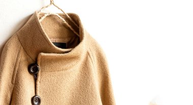 Elbiselerde asılı bej renkli yün palto. Beyaz arka planda asılı. Kapat..
