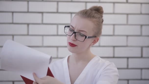 Portrait of office woman in glasses with white shirt and red lips holding folder with papers and reading documents isolated over white background — Stock Video