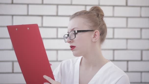 Potret wanita kantoran berkacamata dengan kemeja putih dan bibir merah yang memegang folder dengan kertas dan menulis dalam dokumen yang terisolasi di atas latar belakang putih — Stok Video